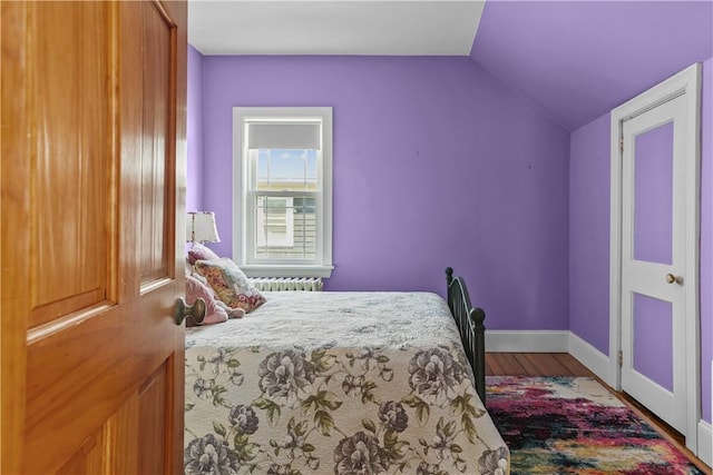 bedroom featuring baseboards, radiator, wood finished floors, and lofted ceiling