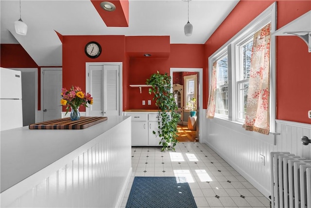 interior space featuring white cabinetry, wainscoting, radiator, and decorative light fixtures