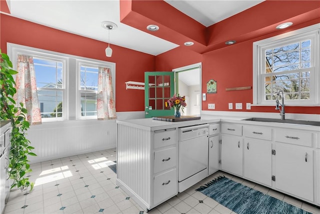 kitchen featuring a sink, white dishwasher, a wainscoted wall, light countertops, and white cabinets