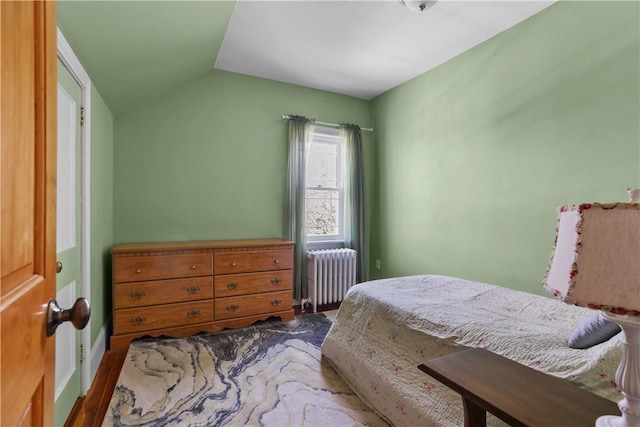 bedroom with radiator heating unit, vaulted ceiling, and wood finished floors
