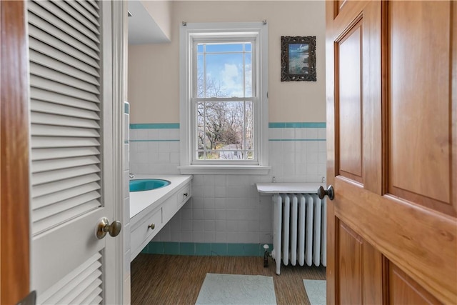 bathroom featuring tile walls, a wealth of natural light, a wainscoted wall, and radiator