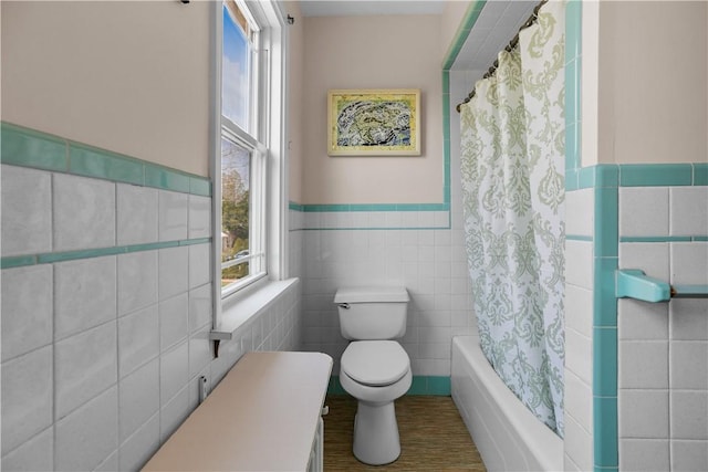 bathroom with toilet, a wainscoted wall, tile walls, and shower / bath combo