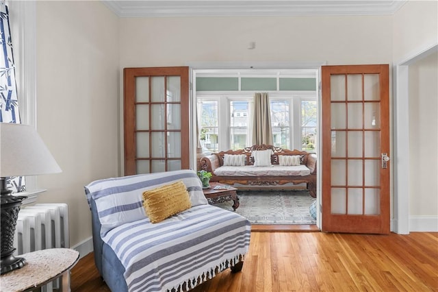 sitting room with baseboards, light wood-type flooring, radiator, and ornamental molding