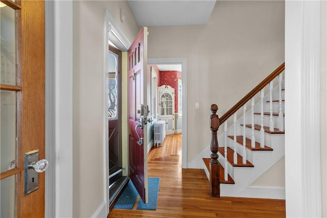 foyer featuring radiator heating unit, wood finished floors, baseboards, and stairs