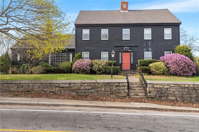 colonial home featuring a chimney and a shingled roof