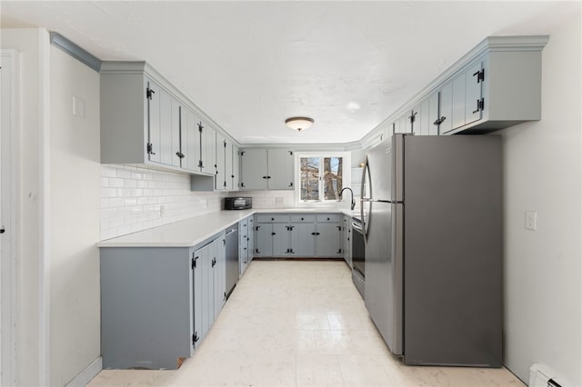 kitchen with decorative backsplash, stainless steel appliances, gray cabinets, light countertops, and a baseboard radiator