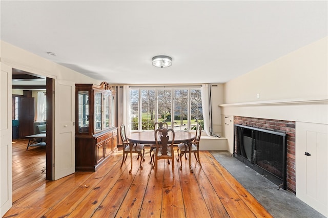dining space featuring light wood-style flooring and a brick fireplace