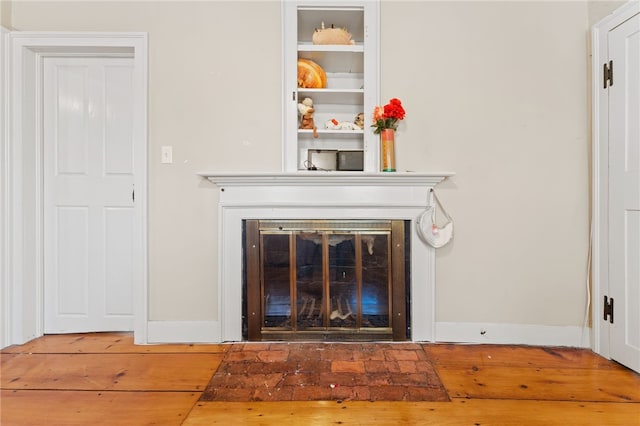 details featuring a glass covered fireplace, wood finished floors, and baseboards