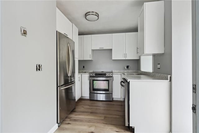 kitchen featuring light wood finished floors, a sink, light countertops, white cabinets, and appliances with stainless steel finishes