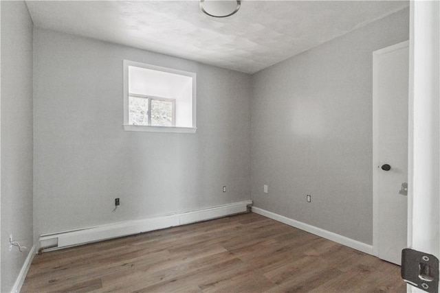 empty room featuring baseboard heating, wood finished floors, and baseboards