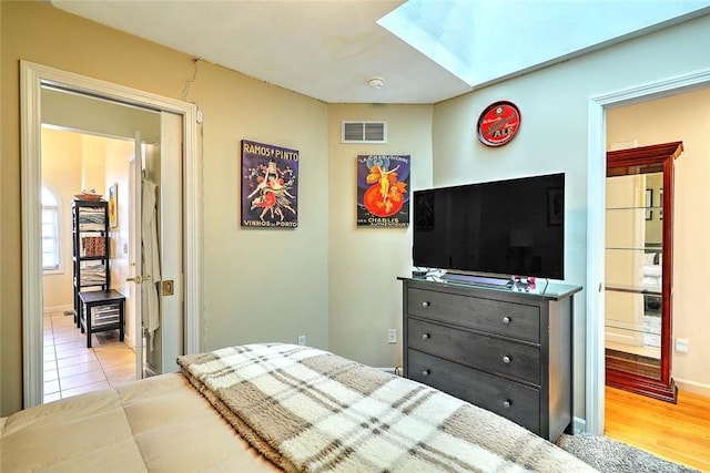 bedroom with a skylight, wood finished floors, ensuite bath, baseboards, and visible vents
