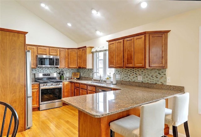 kitchen with a breakfast bar, brown cabinetry, stainless steel appliances, a sink, and a peninsula