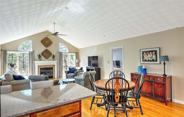 dining room featuring light wood-type flooring, vaulted ceiling, ceiling fan, and a glass covered fireplace