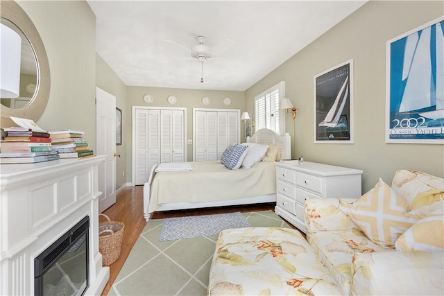bedroom with ceiling fan, baseboards, a glass covered fireplace, tile patterned floors, and two closets