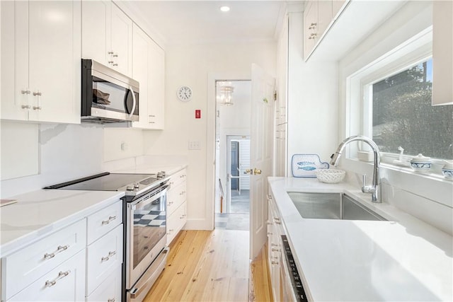 kitchen featuring white cabinetry, light wood-style flooring, a sink, stainless steel appliances, and light countertops