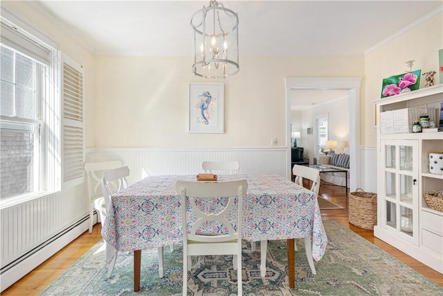 dining room with wood finished floors, an inviting chandelier, a baseboard radiator, a wainscoted wall, and crown molding