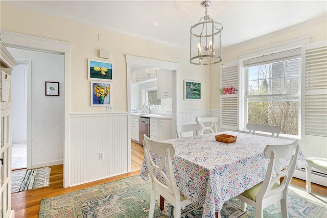 dining room with light wood-style floors, crown molding, a chandelier, and wainscoting