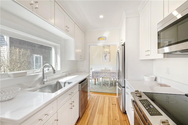 kitchen featuring stainless steel appliances, light wood-style floors, light countertops, a sink, and white cabinetry
