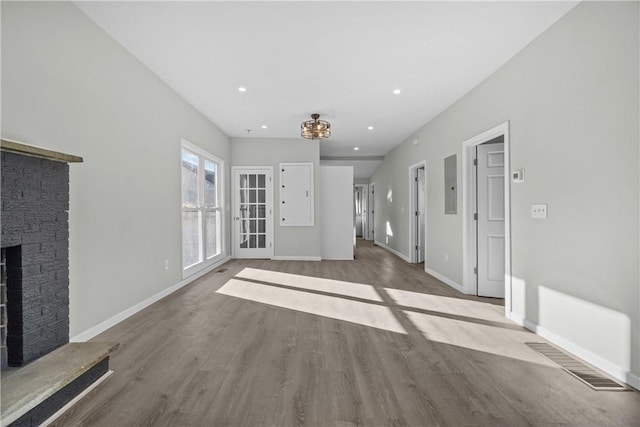 unfurnished living room with wood finished floors, a stone fireplace, electric panel, baseboards, and visible vents