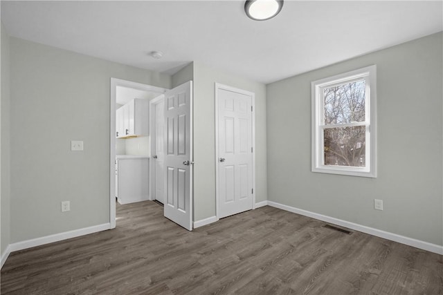 unfurnished bedroom featuring dark wood-type flooring, visible vents, and baseboards