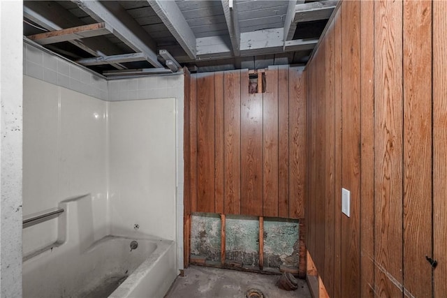 bathroom with a washtub, concrete flooring, and wood walls