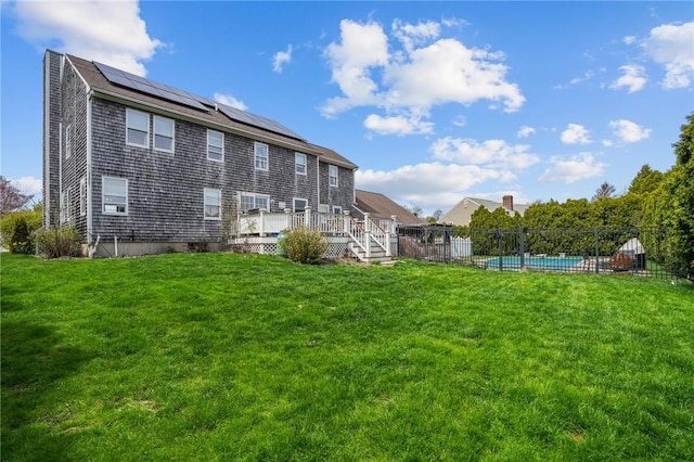 back of house featuring fence, a fenced in pool, a wooden deck, roof mounted solar panels, and a lawn