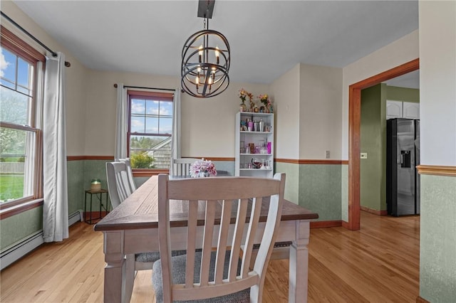 dining area featuring an inviting chandelier, light wood-type flooring, baseboards, wainscoting, and a baseboard radiator