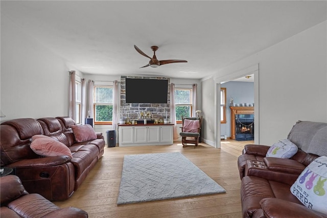 living room with a ceiling fan, light wood-style flooring, and a warm lit fireplace