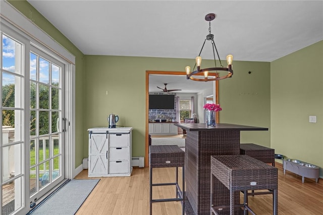 dining area with a baseboard heating unit, light wood finished floors, baseboards, and ceiling fan with notable chandelier