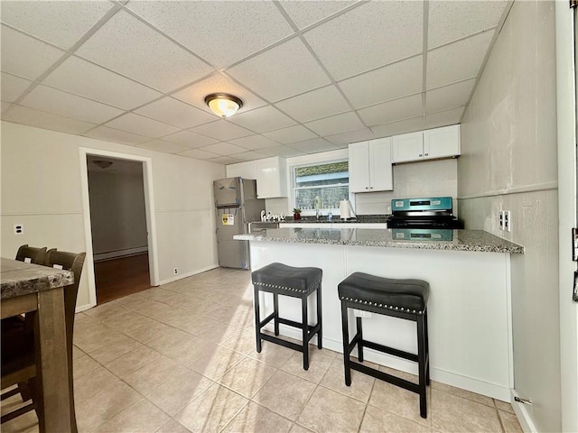 172 Park Ave, Woonsocket, RI 02895 - kitchen featuring electric range, a breakfast bar area, freestanding refrigerator, white cabinetry, and a peninsula