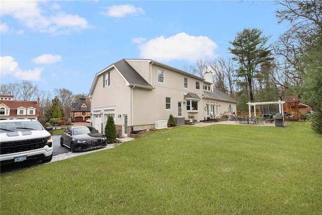 rear view of property featuring a lawn, a garage, stucco siding, and a chimney