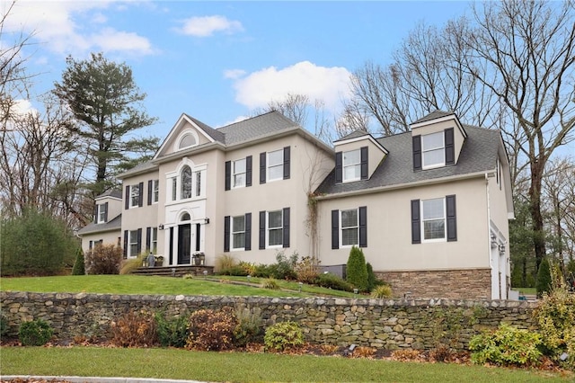 view of front of house with a front yard, stone siding, stucco siding, and a shingled roof