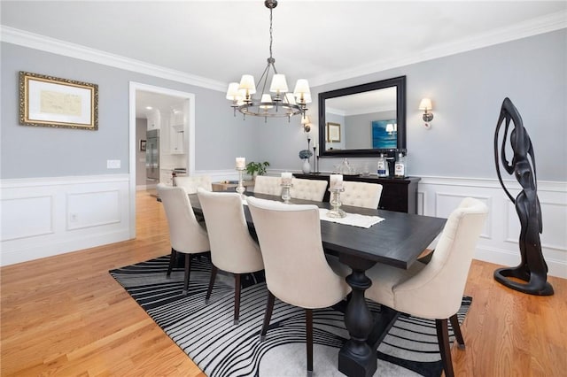 dining area with an inviting chandelier, wood finished floors, a wainscoted wall, and ornamental molding