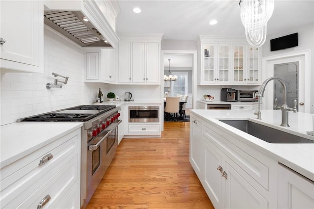 kitchen with a sink, an inviting chandelier, custom range hood, double oven range, and white cabinets