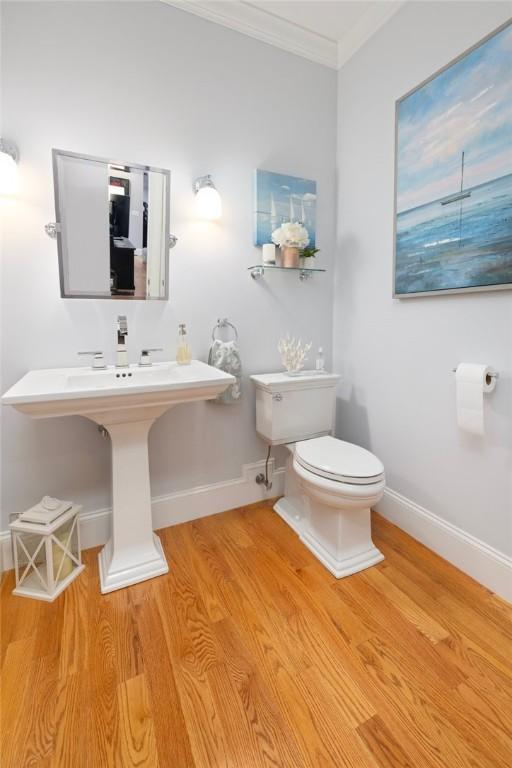 half bathroom with toilet, ornamental molding, wood finished floors, and baseboards