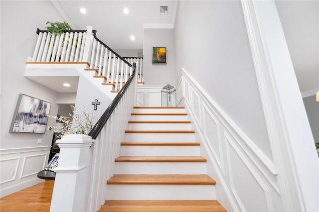 stairway featuring visible vents, wood finished floors, wainscoting, and a decorative wall