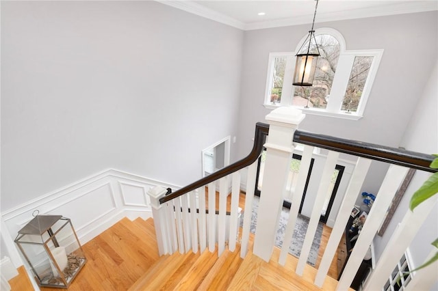 staircase featuring an inviting chandelier, crown molding, a wainscoted wall, a decorative wall, and wood finished floors