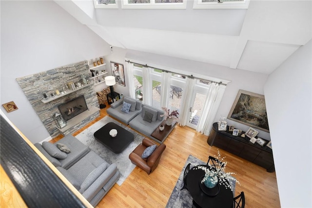 living area featuring vaulted ceiling with beams, wood finished floors, and a stone fireplace