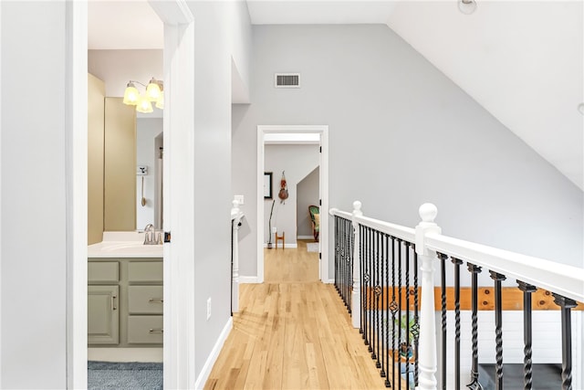 hallway with visible vents, a sink, baseboards, lofted ceiling, and light wood-style floors