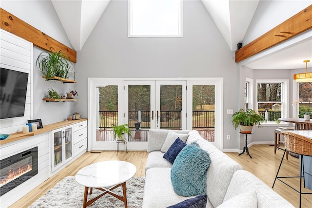 living room with light wood-style flooring, a glass covered fireplace, and high vaulted ceiling
