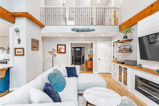 living room with light wood-type flooring, recessed lighting, baseboards, and a high ceiling