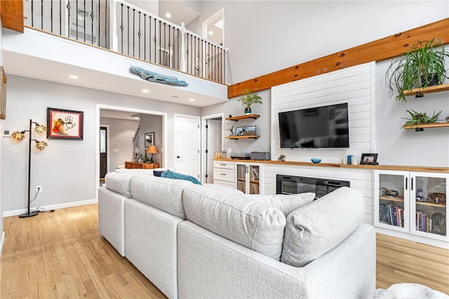 living area featuring light wood-style floors, baseboards, recessed lighting, and a towering ceiling