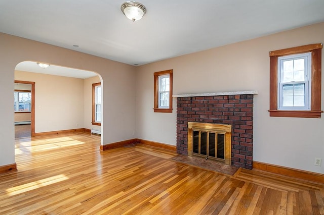 unfurnished living room with arched walkways, a baseboard radiator, a brick fireplace, and hardwood / wood-style flooring