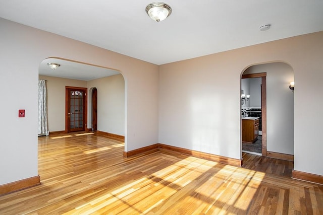 empty room featuring light wood-style floors, arched walkways, and baseboards