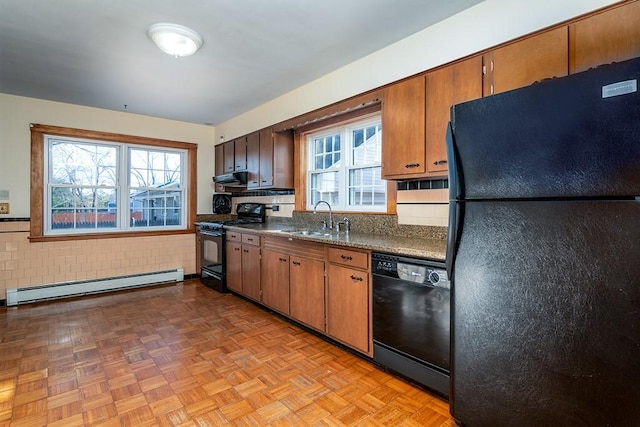 kitchen featuring a sink, dark countertops, black appliances, a baseboard radiator, and exhaust hood