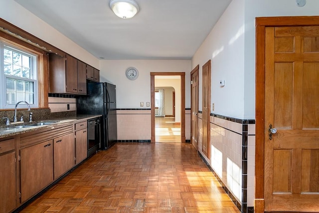 kitchen featuring arched walkways, tile walls, a sink, a wainscoted wall, and black dishwasher