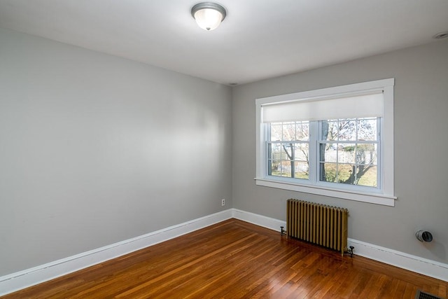 spare room featuring radiator heating unit, baseboards, and dark wood-style floors