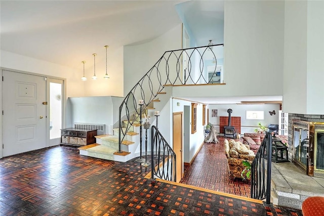 foyer with a high ceiling, a wood stove, stairs, and a brick fireplace