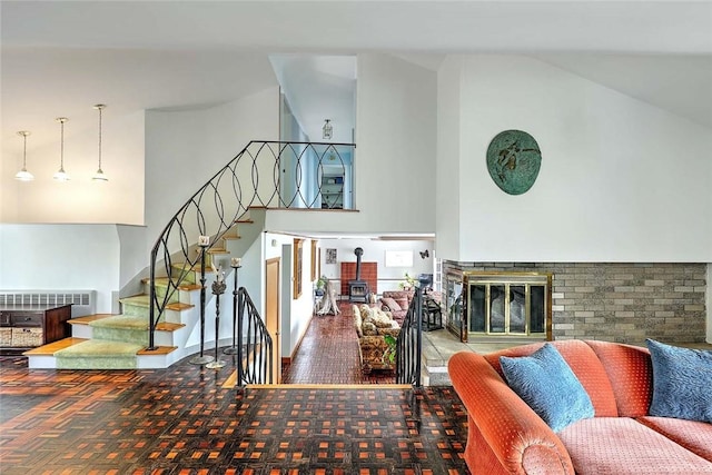 living area with a glass covered fireplace, high vaulted ceiling, a wood stove, and stairs