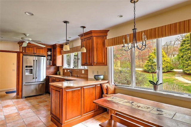 kitchen with a sink, stainless steel fridge with ice dispenser, brown cabinetry, a peninsula, and decorative light fixtures
